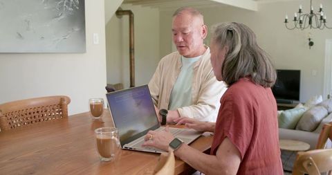 Asian senior couple using laptop at dining table for remote work and planning