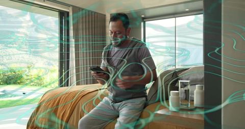 Asian man using smartphone in modern bedroom, relaxing in loungewear with wellness overlay