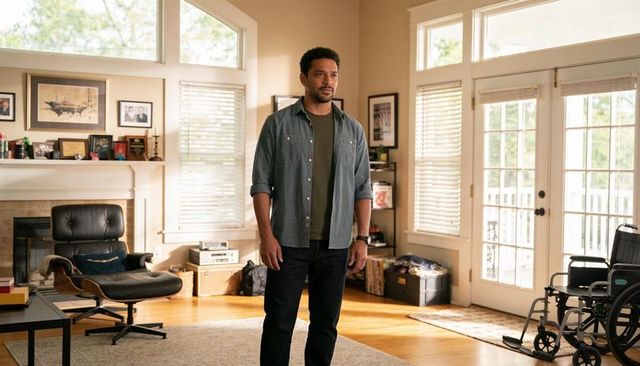 Man standing in sunlit living room with wheelchair by french doors for home recovery