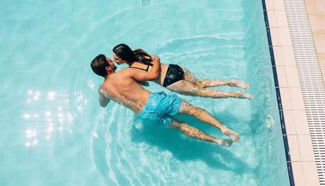 Sunlit pool romance: couple floating and kissing in turquoise water