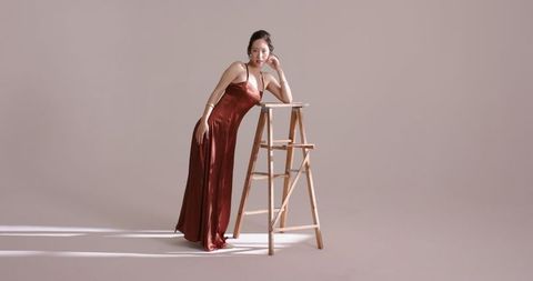 Elegant asian woman in red satin dress leaning on ladder