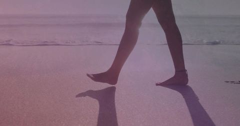 Barefoot woman walking along wet sand with anklet, shoreline reflection and long shadow