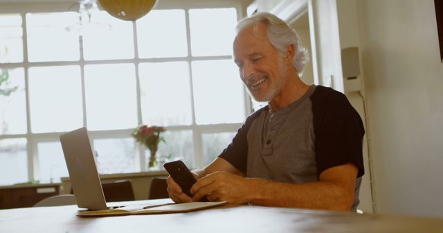 Senior Man Using Smartphone While Working on Laptop in Bright Home Office - Download Free Stock Images Pikwizard.com