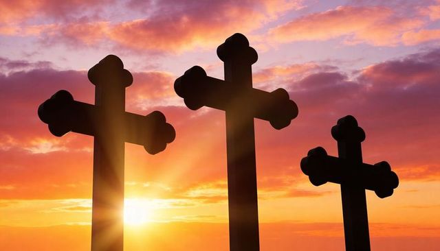 Three trefoil crosses silhouetted at sunrise casting radiant golden rays over dramatic sky