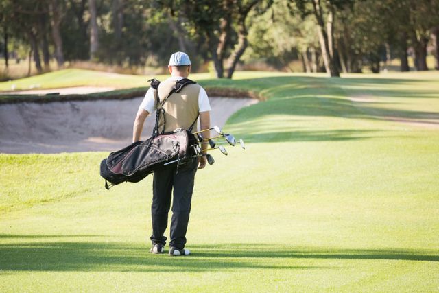 Rear view of sportsman walking with his golf bag on a field