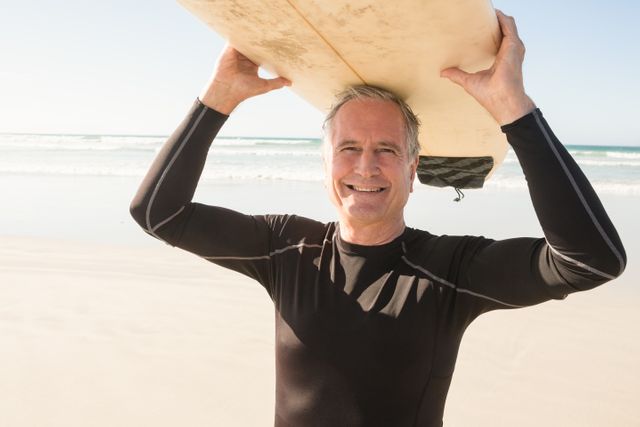 Portarit of smiling senior man carrying surfboard while standing at beach