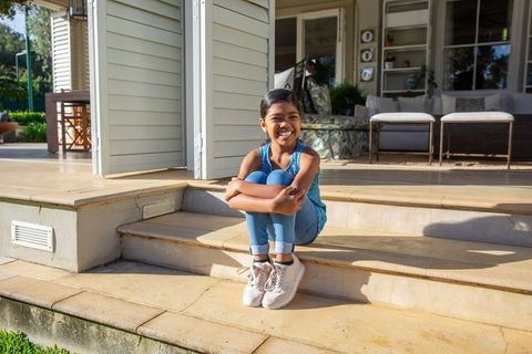 Happy Asian Girl Sitting on Sunlit Porch Steps
