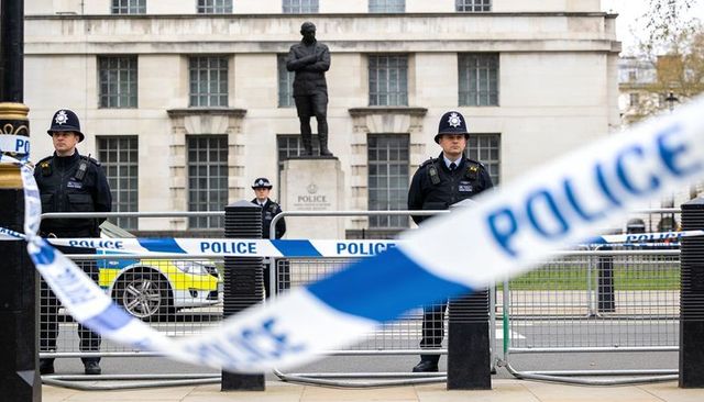 Uniformed police officers guarding cordoned civic plaza with police tape and statue