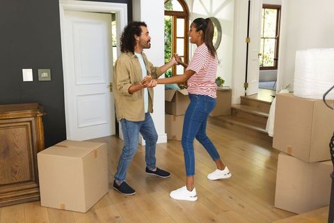 Young couple dancing while moving into new home among cardboard boxes