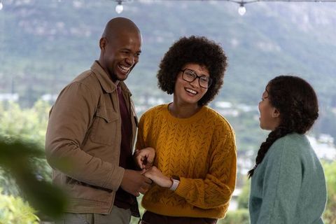 Laughing family holding hands on terrace under string lights with hillside view