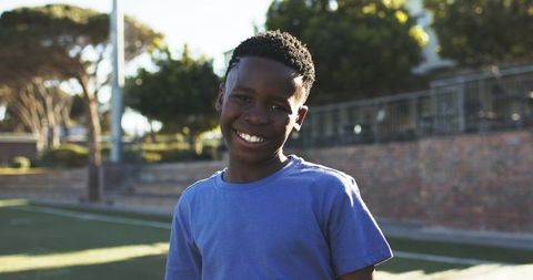 Smiling african teen boy wearing blue t-shirt on outdoor turf at golden hour