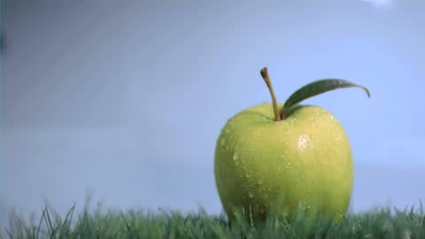 Green Apple with Water Droplets on Grass in Slow Motion