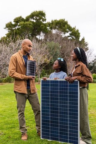 Diverse family learning solar energy with handheld and large photovoltaic panels outdoors