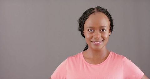 Confident african woman smiling and posing in pink top on neutral gray backdrop