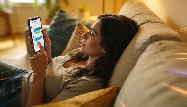 Reclining woman scrolling messages on smartphone cozy sofa home evening relaxation