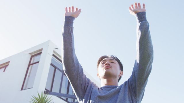 The video shows a young man with a joyful expression, jumping with his arms raised outside a modern building. This visual can be used for promoting active lifestyle, fitness, well-being, happiness, self-care, outdoor activities, and spending time at home. Ideal for health and wellness blogs, lifestyle magazines, advertising campaigns, and social media posts directed at promoting positive living and joyful activities.