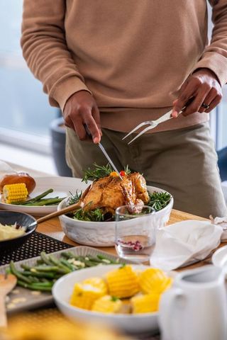 African american man carving golden roasted chicken at cozy sunlit family dinner table