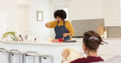 Diverse couple baking at breakfast bar, woman cracking eggs in modern kitchen