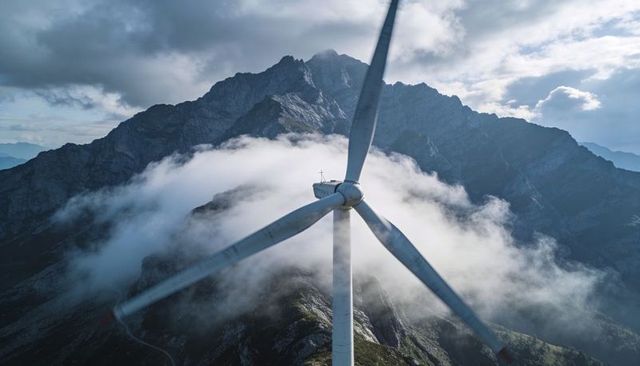 Wind turbine towering over misty alpine ridge and rocky peaks highland renewable energy