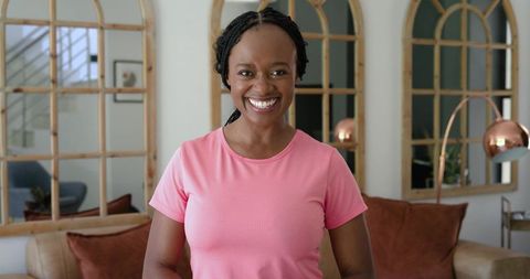 African american woman smiling in contemporary living room wearing pink t-shirt