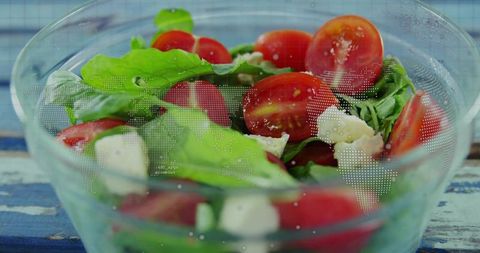 Vibrant cherry tomato mozzarella arugula salad in glass bowl on rustic blue wooden table