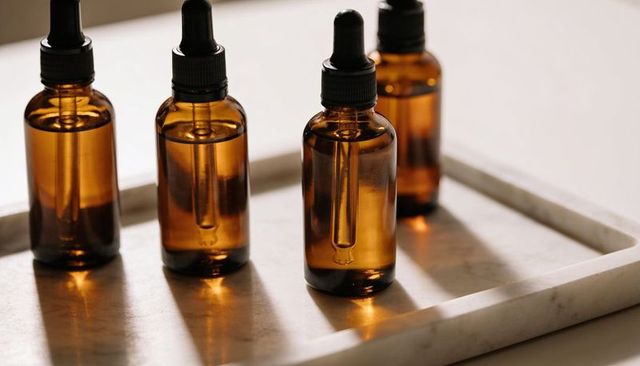 Amber glass dropper bottles on marble tray catching warm natural light for beauty branding