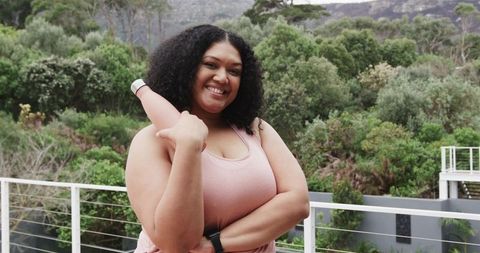 Confident african american woman smiling holding yoga mat on balcony with lush greenery