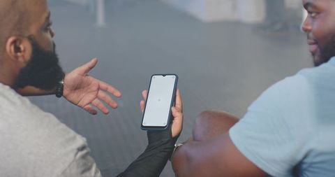 African men coaching at gym sharing workout plan on smartphone during training
