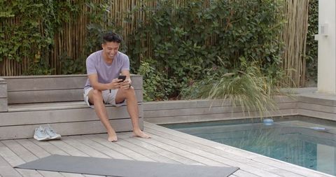 Man relaxing by pool checking smartphone