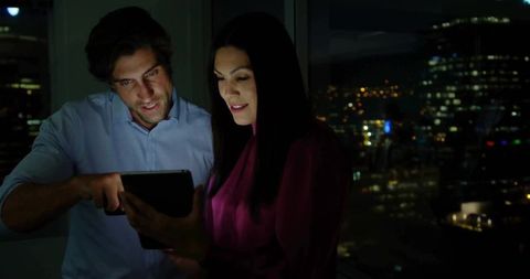 Professionals Collaborating on Tablet with City Skyline at Night