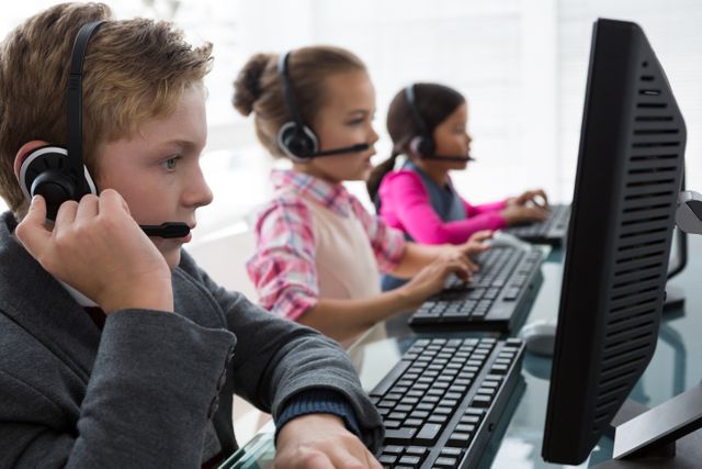Children wearing headsets and working on computers in an office environment, simulating customer service representatives. This image can be used to illustrate concepts of early career education, technology use among children, teamwork, and the importance of communication skills. Ideal for educational materials, business training programs, and articles on child development and professional skills.