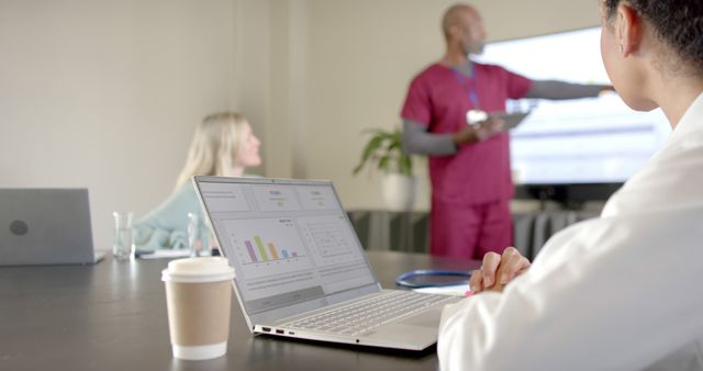 Healthcare professionals in a meeting room, with a focus on a laptop screen displaying analytical data, engaging in a presentation. This image can be used for depicting medical seminars, healthcare analysis, corporate training, or team collaboration in healthcare settings. It emphasizes teamwork, technology use in healthcare, and professional development.