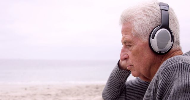 Thoughtful retired man listening to music on the beach