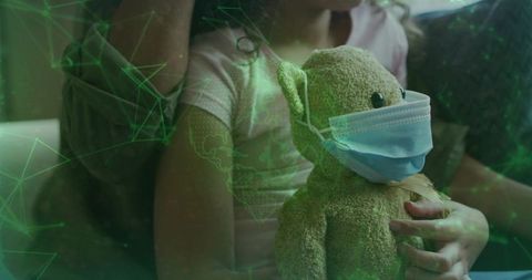 Child holding masked teddy while parent comforting on sofa with green network overlay