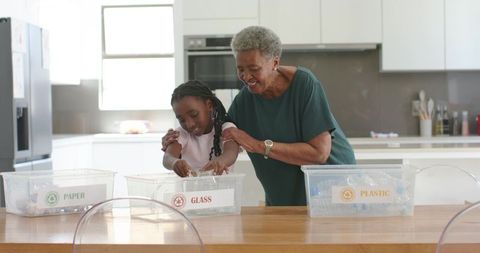 African american senior woman teaching granddaughter recycling, sorting paper glass plastic in kitch