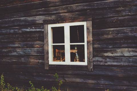 Rustic cabin window framed by weathered wood showcasing vintage oil lamps and warm glow