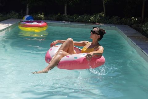 Woman relaxing on pink donut float in backyard pool under bright summer sunlight