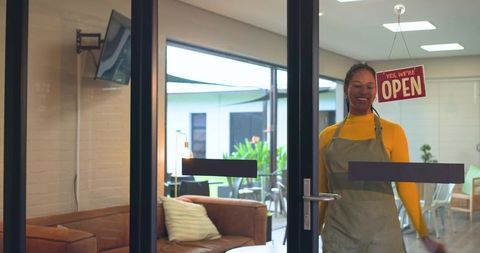 African american barista opening cafe door and smiling, modern cozy storefront with patio greenery
