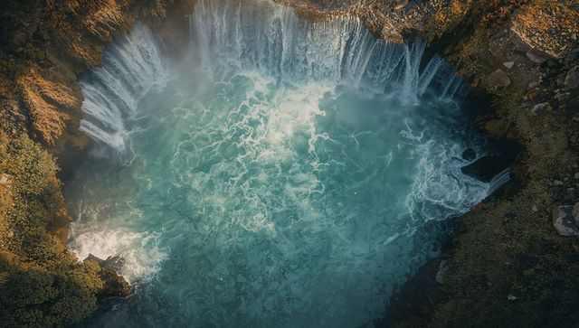Semicircular waterfall cascading into turquoise plunge pool with misty foam in canyon