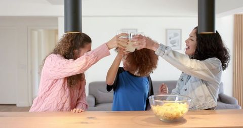 Female friends toasting with drinks at kitchen counter during casual home gathering