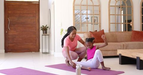 African mother guiding daughter during home yoga stretch in cozy living room wellness