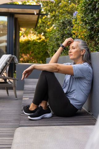 Contemplative senior woman sitting on deck in activewear with smartwatch, outdoor relaxation