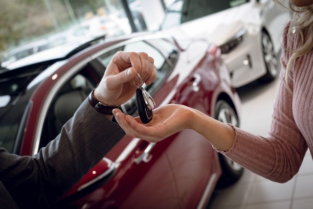 Salesman handing car keys to female customer in showroom. Ideal for illustrating car sales, customer service, automotive industry, and business transactions. Useful for websites, brochures, and advertisements related to car dealerships and automotive services.