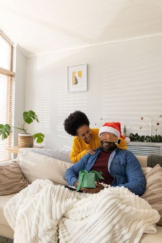 African american couple sharing christmas surprise on sofa with santa hat and green gift