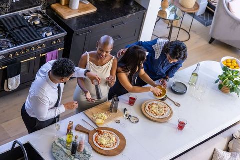 Friends making homemade pizzas on marble island in modern minimalist kitchen