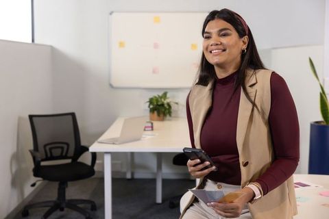Professional woman using smartphone while holding color swatches in modern office