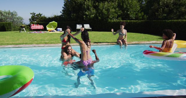 Diverse group of friends having fun playing in swimming pool. hanging out and relaxing outdoors in summer.