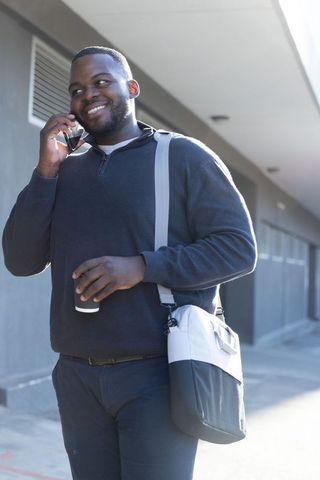 African american man walking and talking on phone holding coffee with shoulder bag