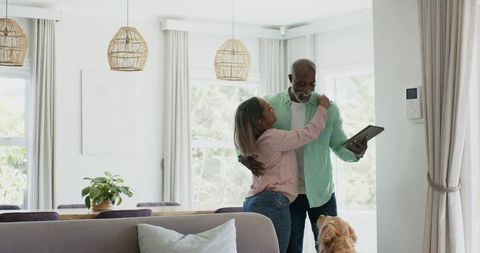 Senior couple embracing in sunlit modern living room with tablet and golden retriever