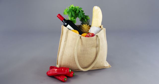 Eco-friendly reusable grocery bag containing fresh produce like bell peppers, pineapple, and a baguette. Bottle of wine adds touch of luxury. Use for sustainability, healthy lifestyle, or grocery shopping themes.